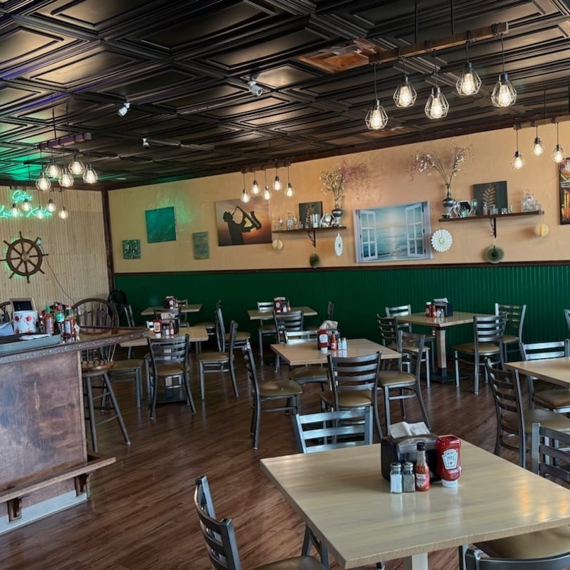 Empty restaurant dining room with wooden tables, chairs, and nautical-themed decor.